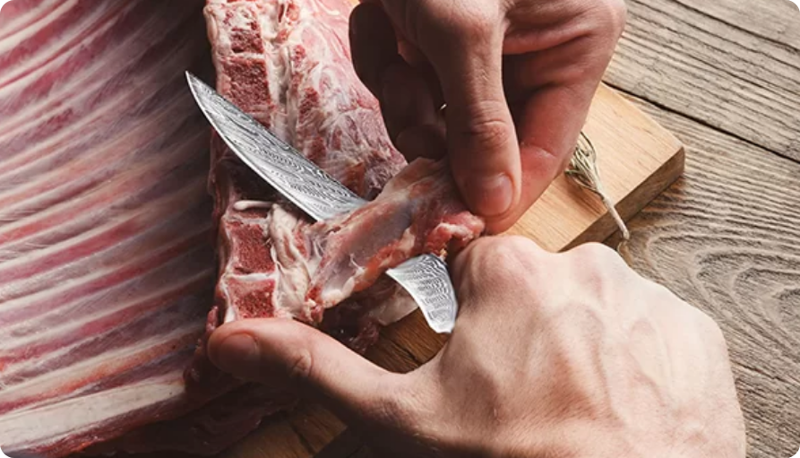 Eine Person nutzt ein scharfes Messer, um Fleisch von einem Rippenstück auf einem hölzernen Schneidebrett zu schneiden. Die Hände arbeiten präzise, um das Fleisch von den Knochen zu lösen.