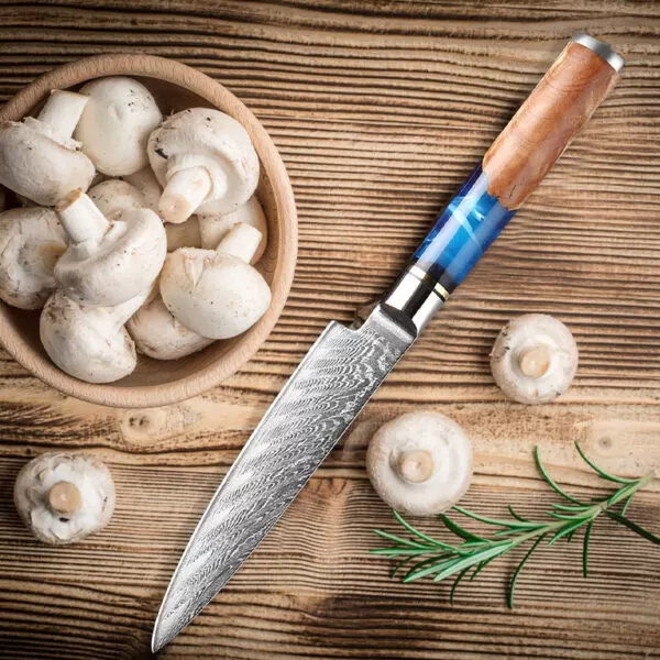 Ein Holzschneidebrett mit einer Schüssel voller frischer Champignons und einem Messer mit einem Griff aus Holz und blauem Harz. Die Kombination aus den frischen Pilzen und dem hochwertigen Messer vermittelt eine Atmosphäre von kulinarischer Vorbereitung und Präzision.