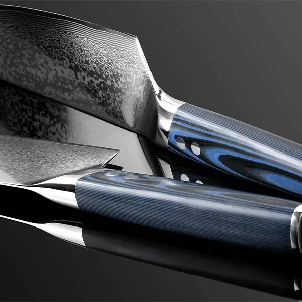 Zwei japanische Küchenmesser mit blauen Griffen und kunstvoll gemusterten Klingen liegen auf einer spiegelnden, schwarzen Oberfläche. Die Klingen zeigen ein detailliertes Damastmuster, das die hohe Qualität und das handwerkliche Können der Messer unterstreicht.