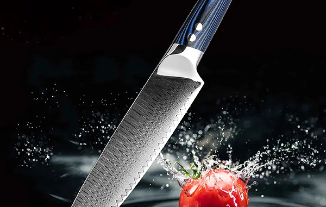 Kochmesser The Blue Knife gallery 3 Ein japanisches Küchenmesser mit einer kunstvoll gemusterten Klinge und einem blauen Griff wird vor einem spritzenden Tomatenhintergrund gezeigt. Das Messer schwebt über einer im Wasser aufschlagenden Tomate, was die Schärfe und Präzision der Klinge betont.